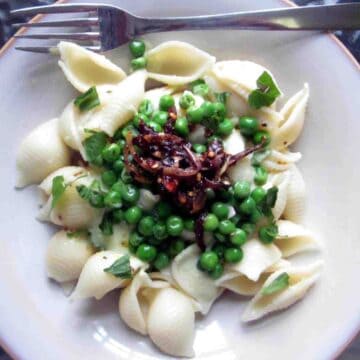 Description: A plate with pasta, peas, and yogurt sauce on it.