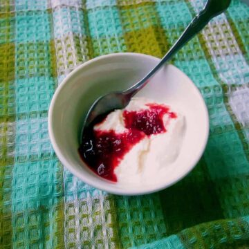 A lactose-free bowl of yoghurt with a spoon on a tablecloth.