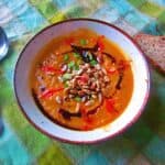 A bowl of roasted squash and carrot soup with seeds and a piece of bread.