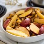 Apples and mushrooms in a white bowl on top of a stove, sprinkled with paprika.