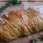 A loaf of rosemary sourdough bread with rosemary sprigs on a cutting board.