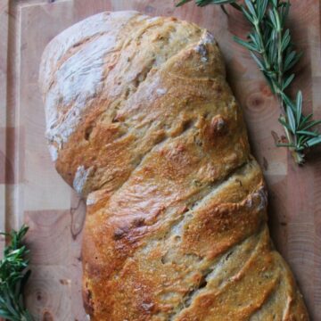 Italian sourdough bread on cutting board with rosemary branches
