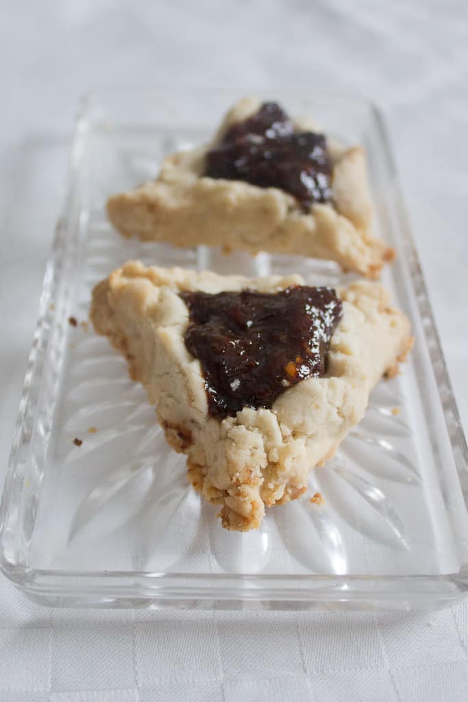 A glass plate with two prune hamantaschen on it.