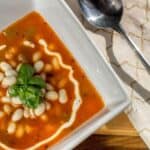 A bowl of Serbian white bean soup with sour cream and basil.