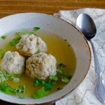 Homemade matzo ball soup with spoon on checkered napkin.