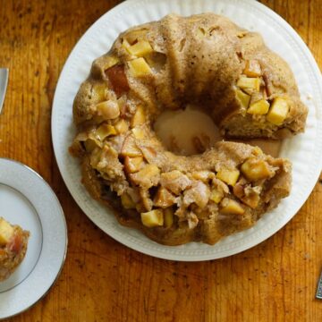 An apple bundt cake with olive oil, served on a plate with a missing slice.