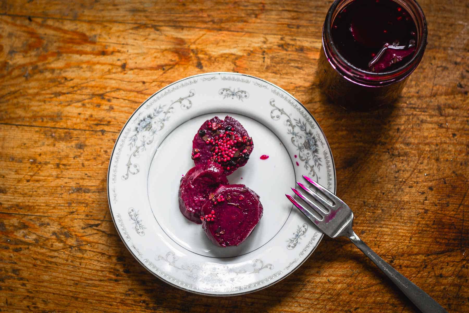 Overhead view of pickled beets on plate beside jar.