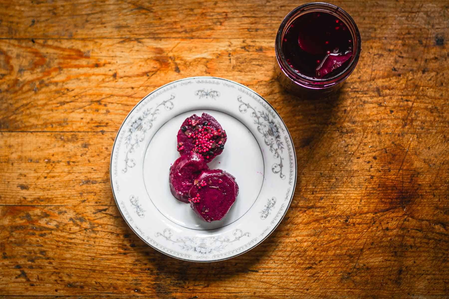 Overhead view of pickled beets on plate beside jar.