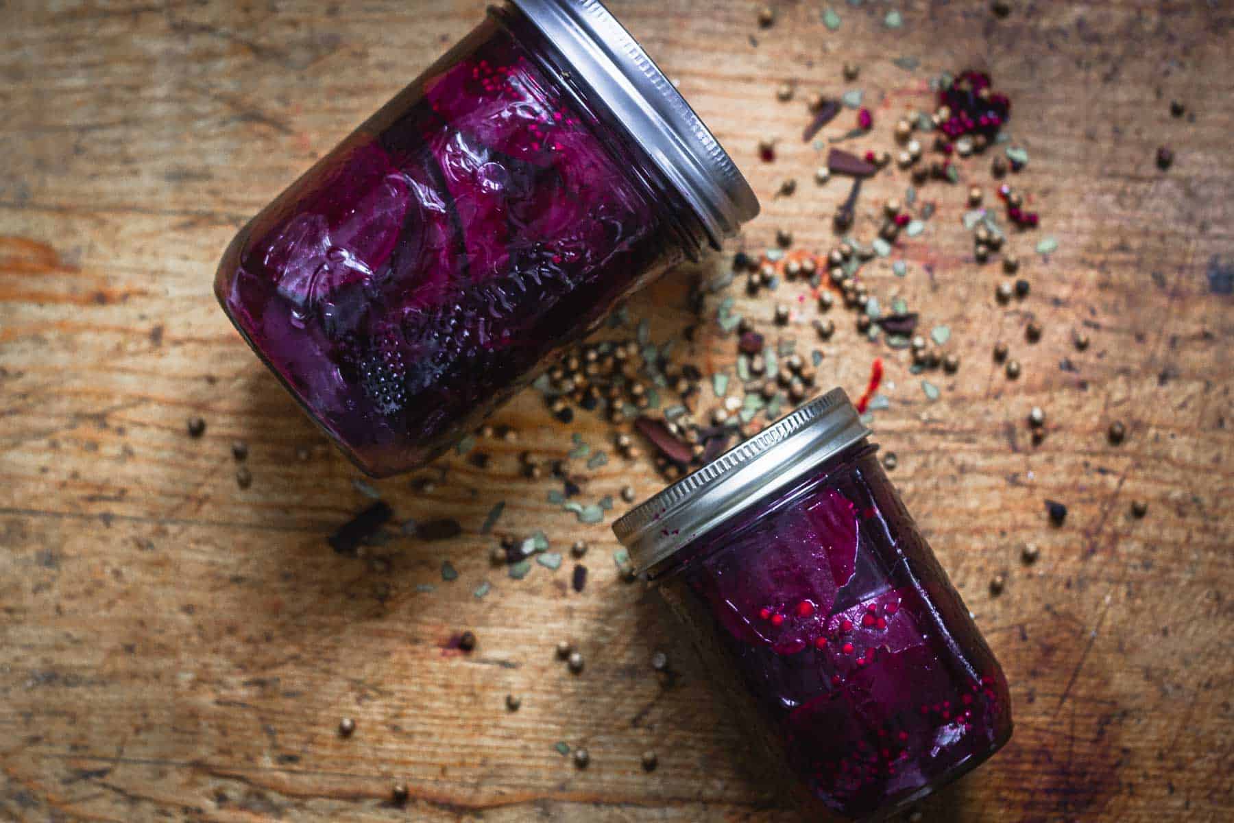 Overhead view of two jars of pickled beets, lying on a wooden surface.