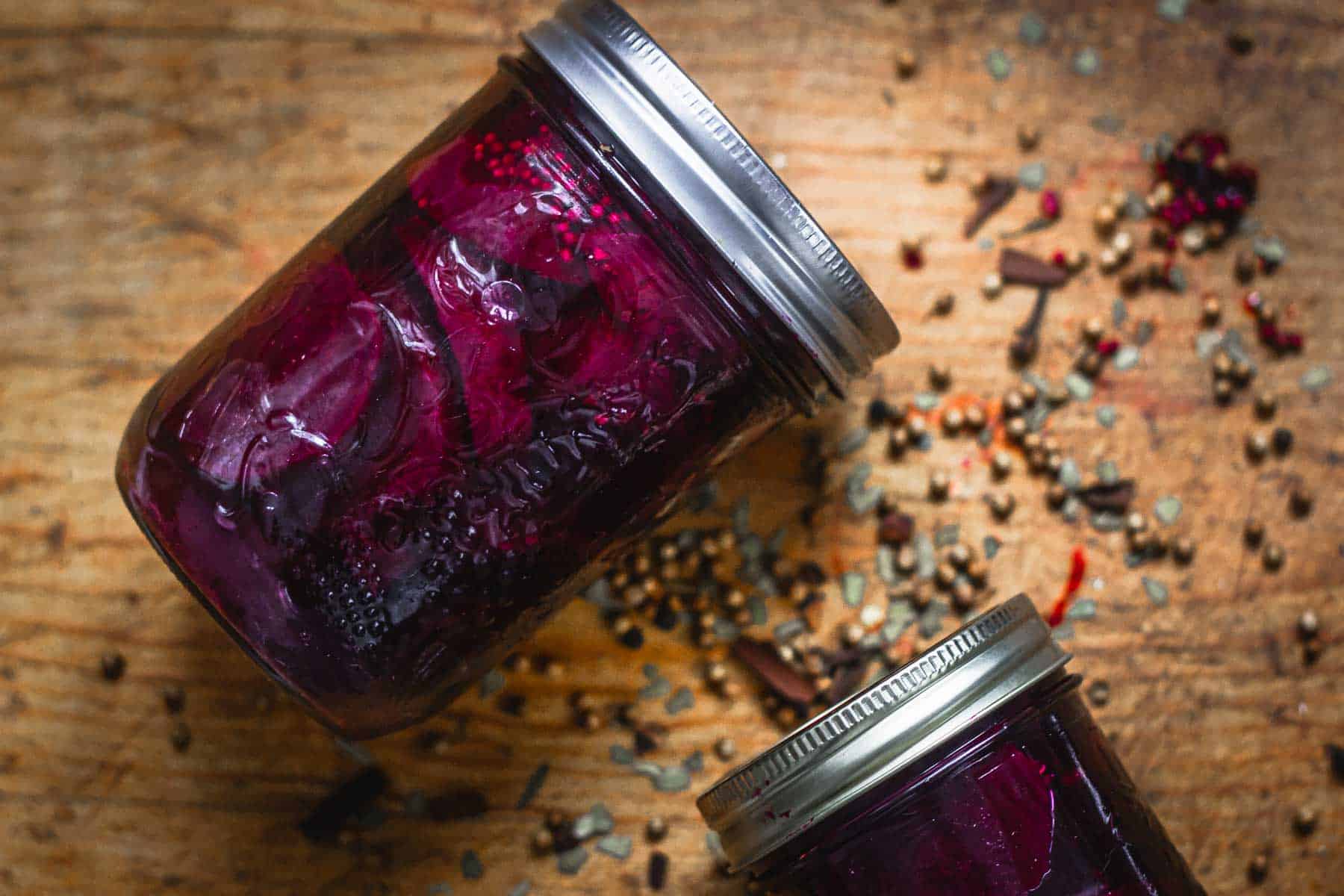 Overhead view of two jars of pickled beets, lying on a wooden surface.