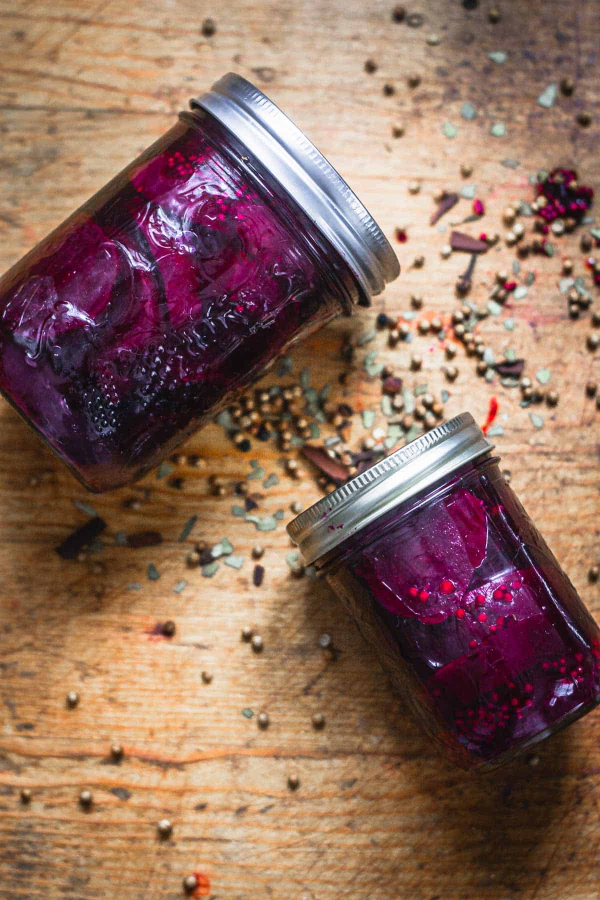 Overhead view of two jars of pickled beets, lying on a wooden surface.