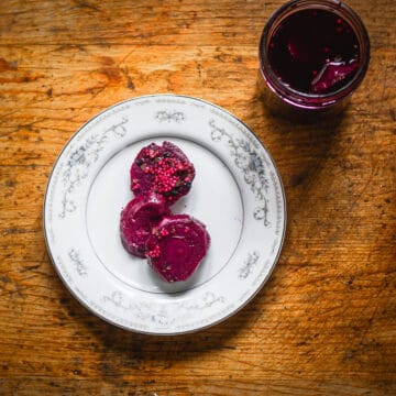 Overhead view of pickled beets on plate beside jar.