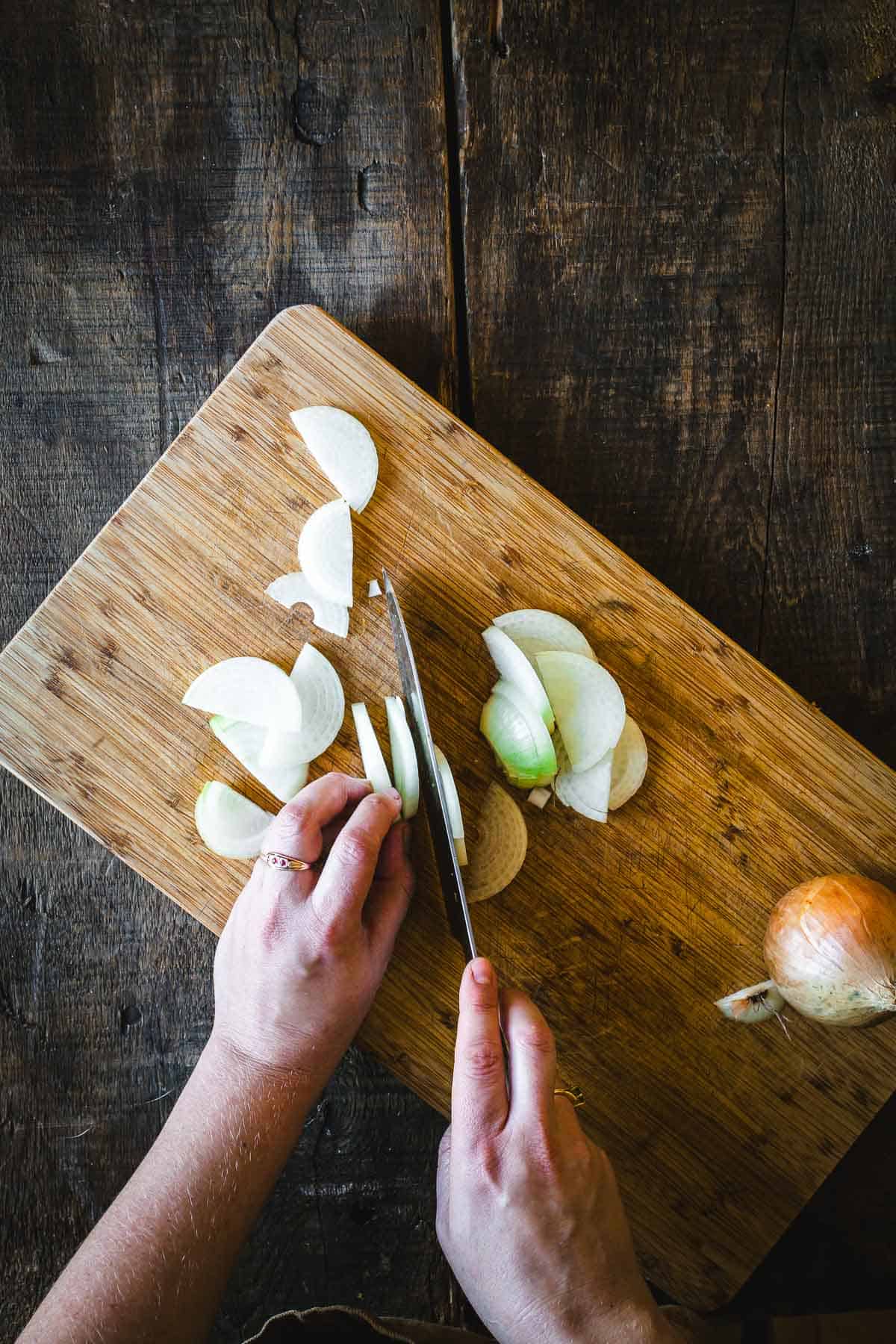 A person making garlic scape pickles on a wooden cutting board.