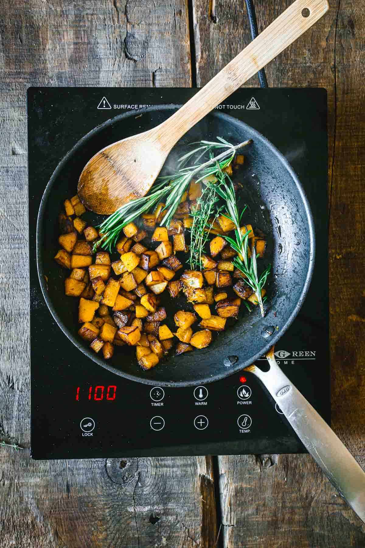 A frying pan filled with vegetables, including garlic scape pickles, and a wooden spoon.