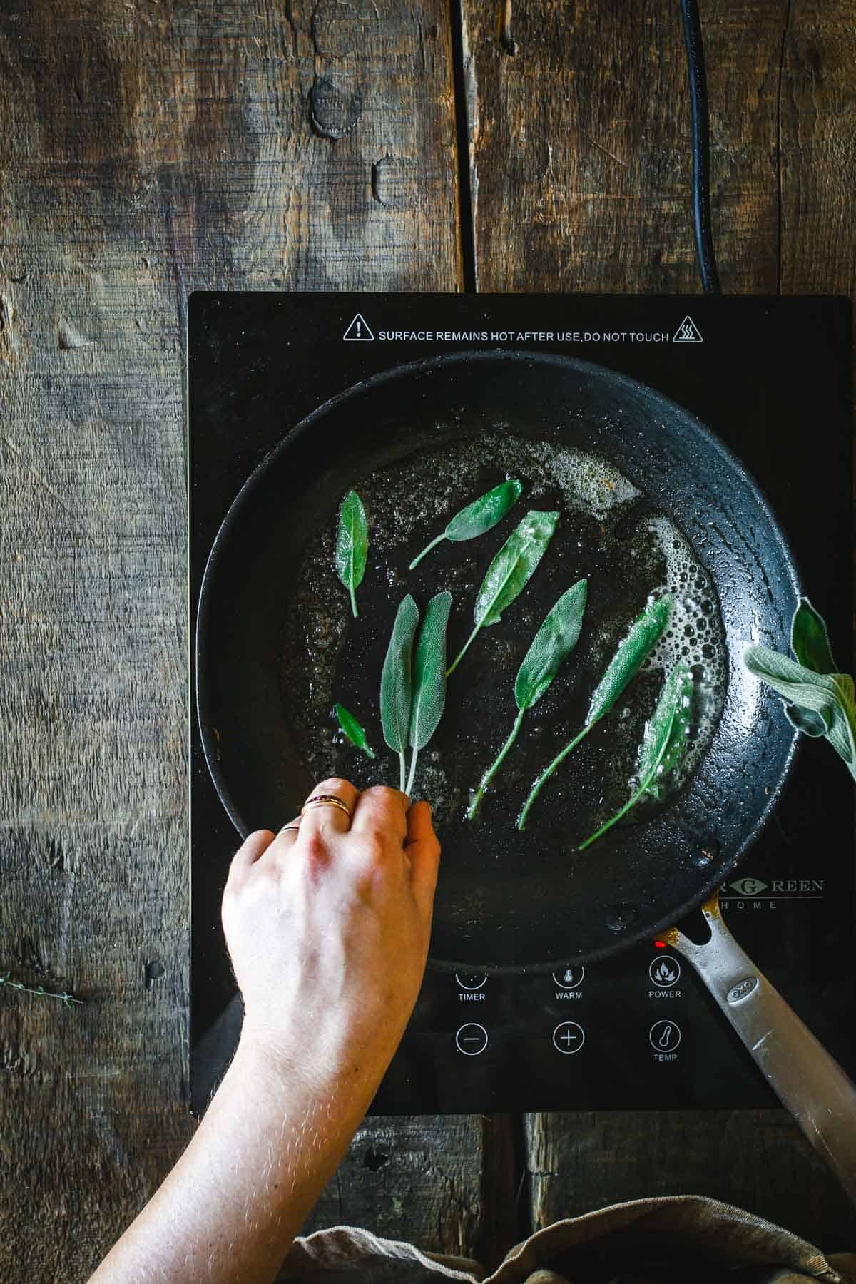 A person is preparing sage leaves in a frying pan with garlic.