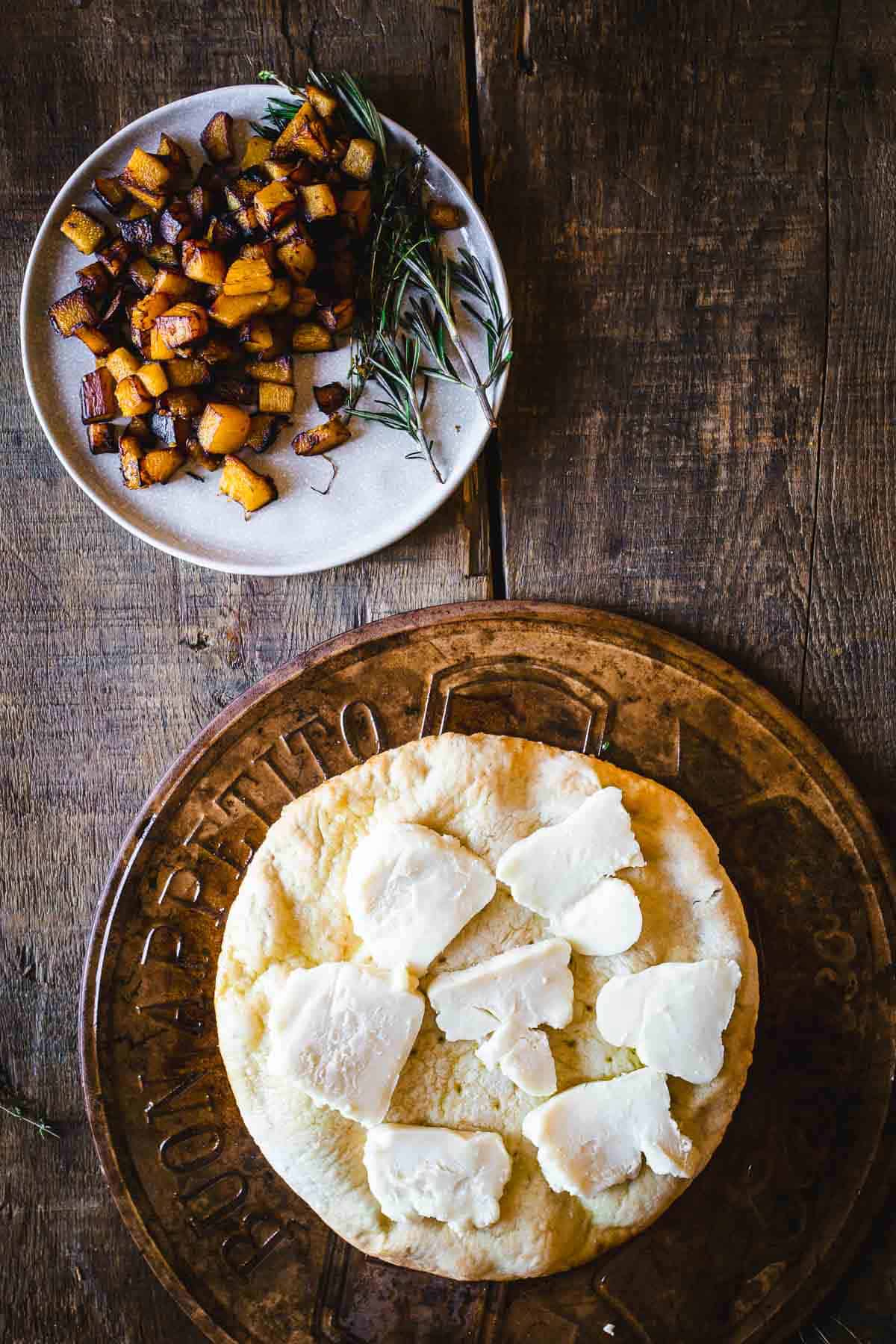 A pizza with cheese, roasted pumpkin, onions and sage on a wooden plate.