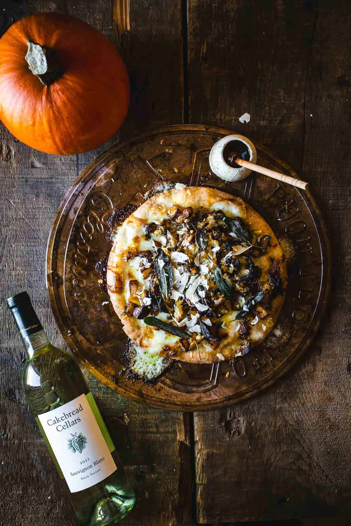 A pizza on a plate next to a bottle of wine.
