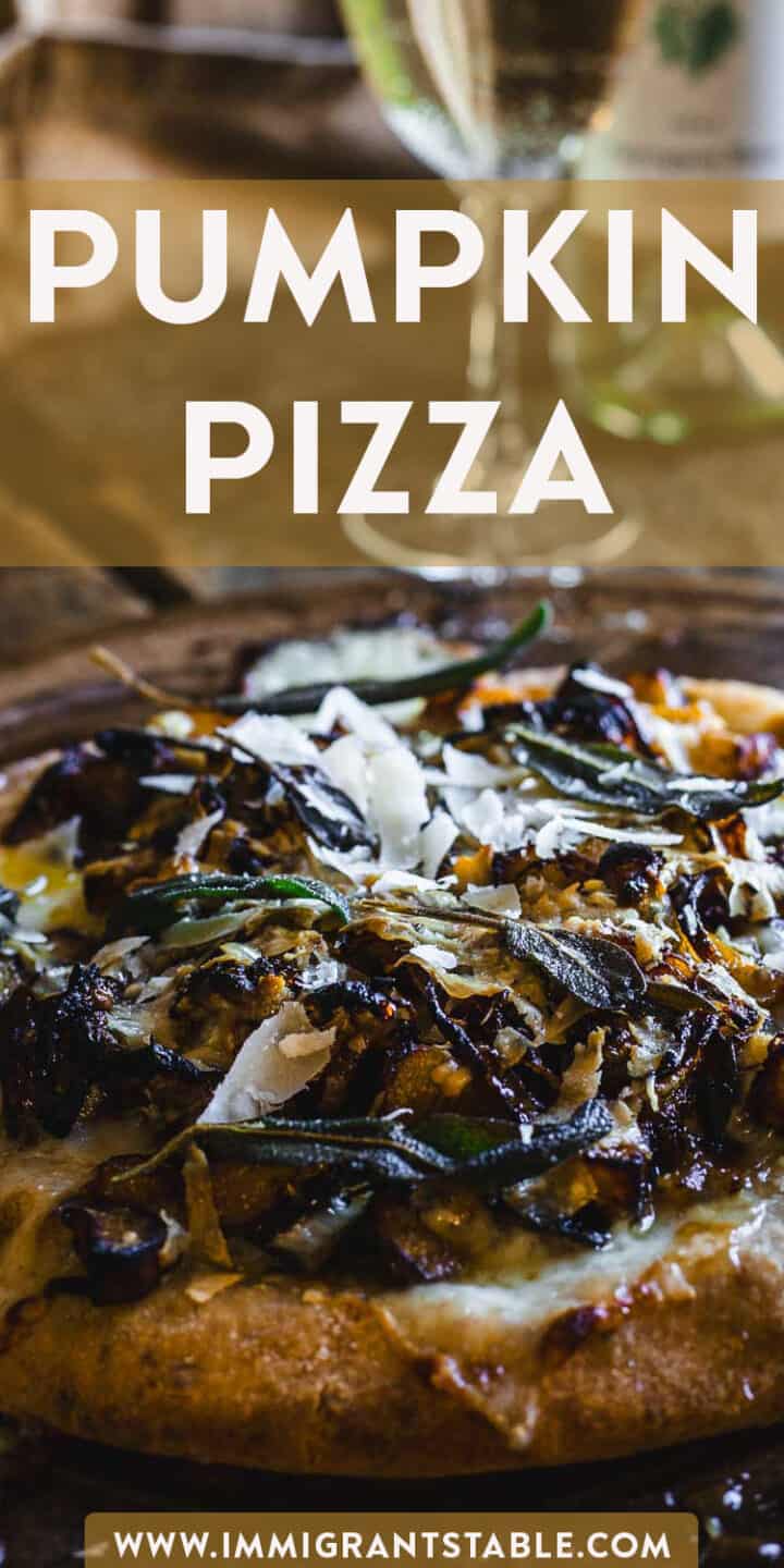 A pumpkin pizza on a wooden table with a glass of wine and garlic scape pickles for added flavor.
