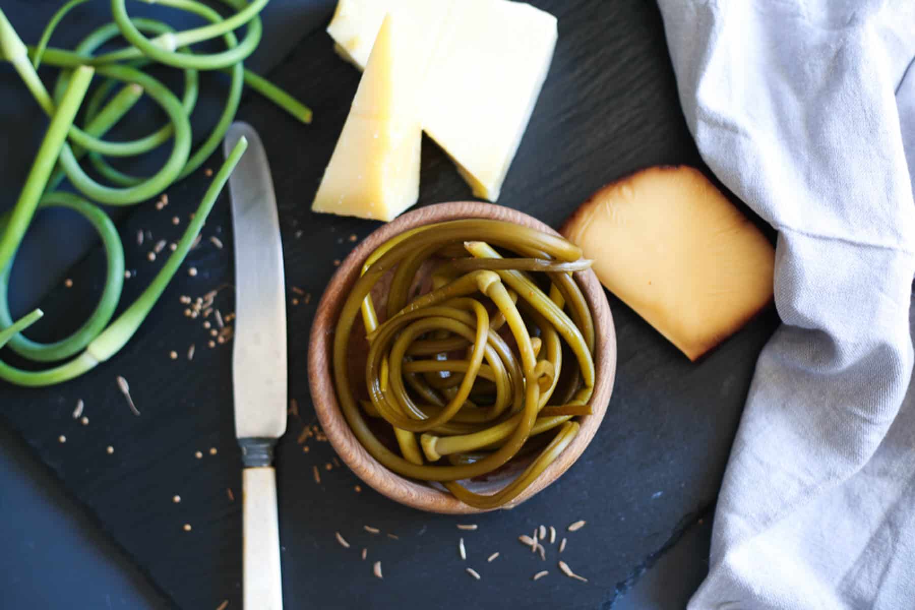 A bowl of green beans with garlic scape pickles and a knife.