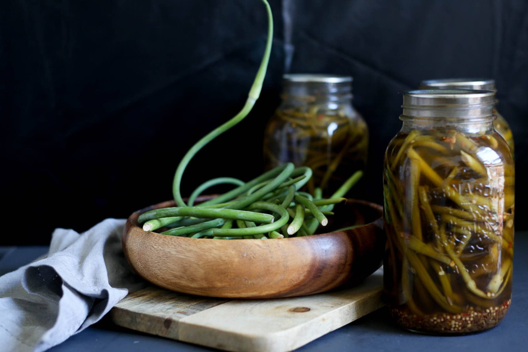 Jars of garlic scape pickles on a wooden cutting board.