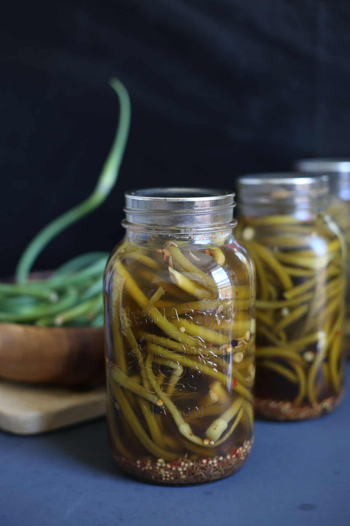 Three jars of garlic scape pickles on a table.