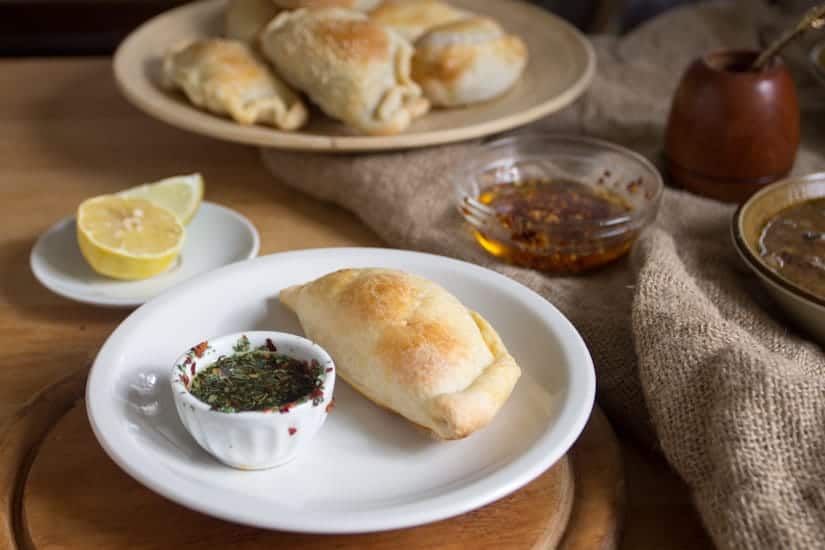 empanada on a plate with dipping sauce, plate full of empanadas in background, matte