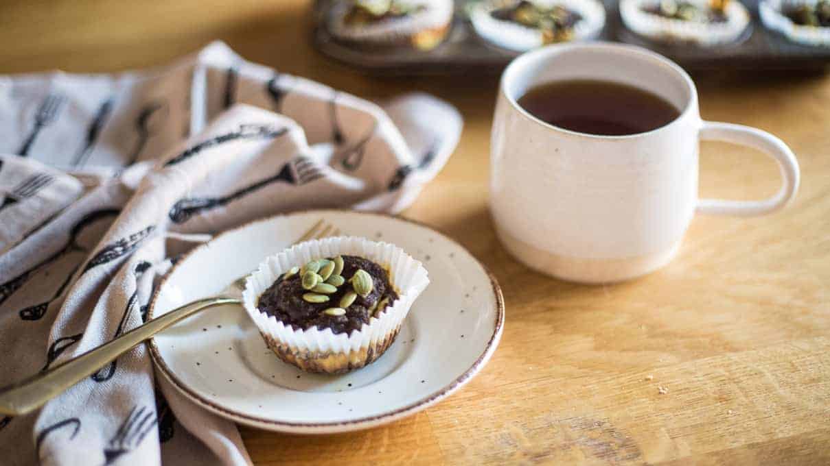 Pumpkin muffin on a plate with a cup of tea nearby.