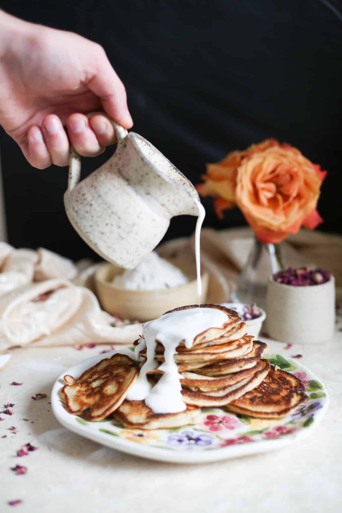 A person pouring gluten-free cream over Russian pancakes on a plate.
