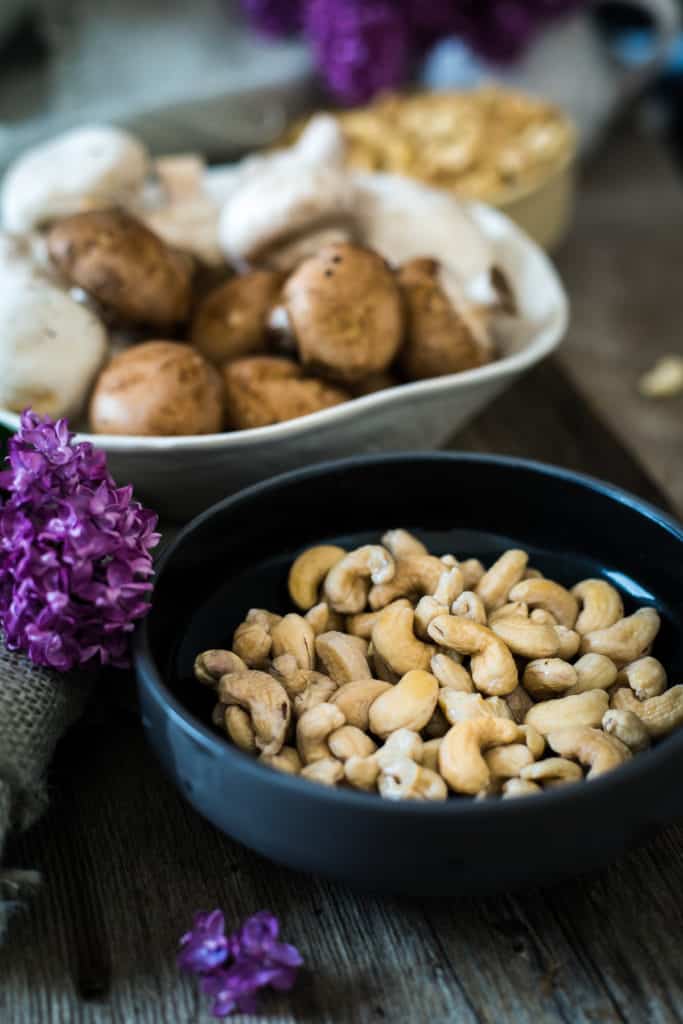 Vegan pasta primavera with cashews, mushrooms, and flowers on a wooden table.