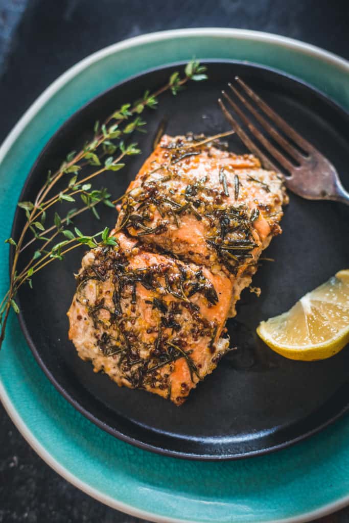 Close up on pan-fried Sockeye salmon recipe with mustard, honey and wild herbs on plate with lemon and fork