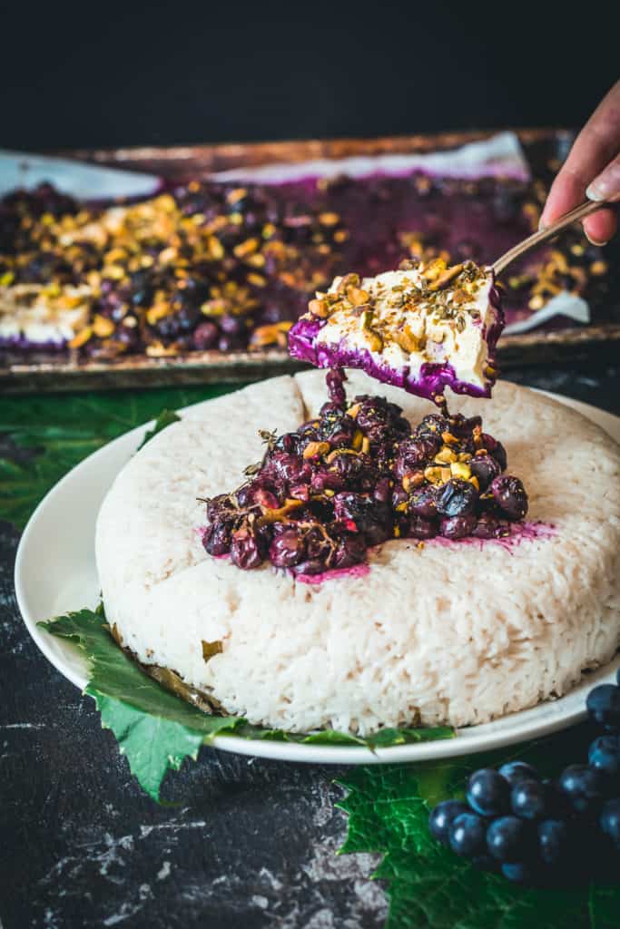 Spoon placing cooked grape sauce and pistachios on rice