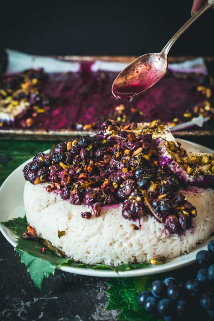 Spoon placing cooked grape sauce and pistachios on rice