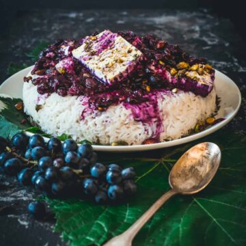 Rice topped with cooked grape sauce and pistachios and feta, spoon in front