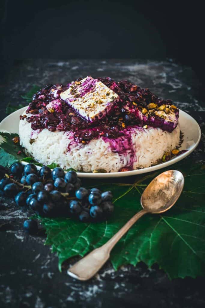 Rice topped with cooked grape sauce and pistachios and feta, spoon in front