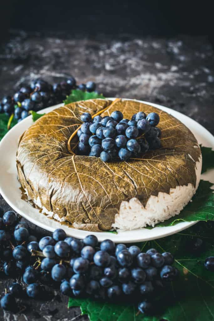 Rice topped with grape leaf and fresh grapes, resting on a large platter and decorated with grapes