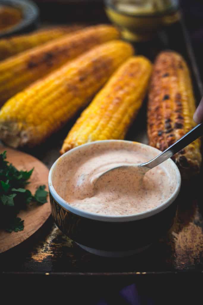spoon in sauce, corn in background