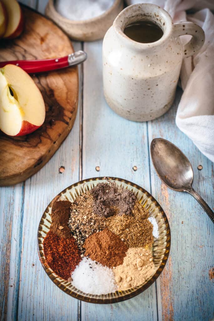 A bowl of spices next to an apple appetizer on a wooden table.