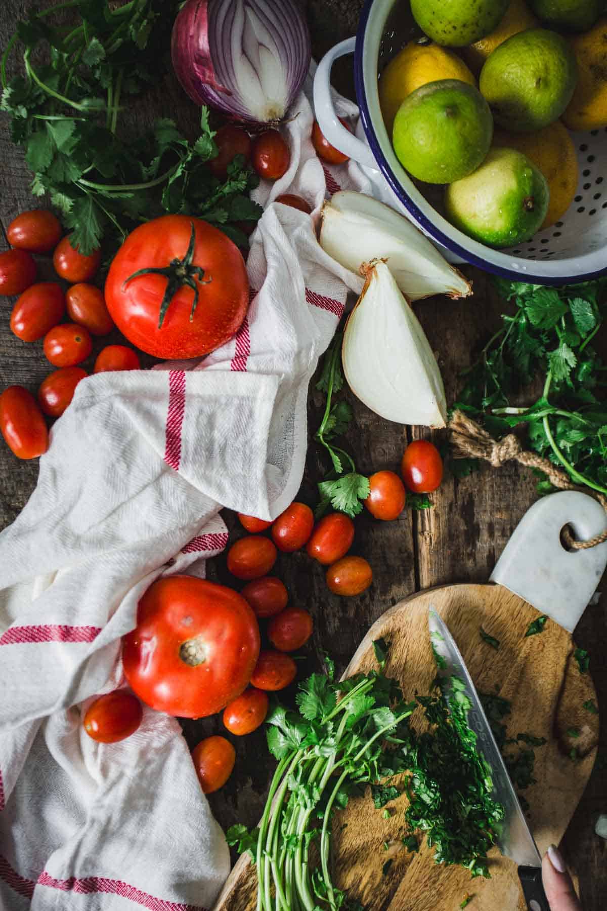 Assorted fresh vegetables and herbs laid out on a wooden surface, including tomatoes, lemons, onions, and parsley, with a focus on natural ingredients for Colombian empanada sauce cooking.