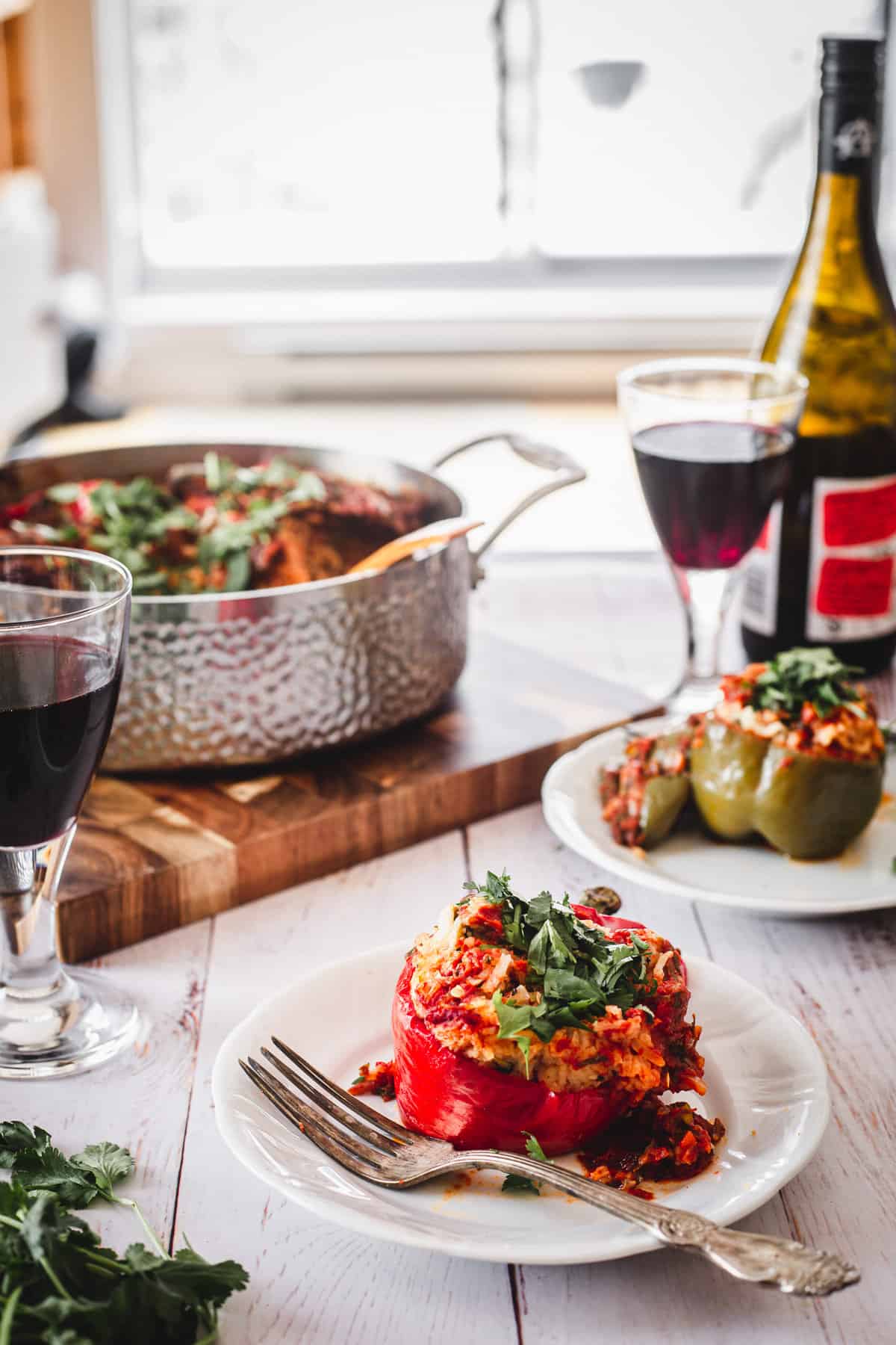 two stuffed peppers, wine glasses, wine bottle and pot with peppers