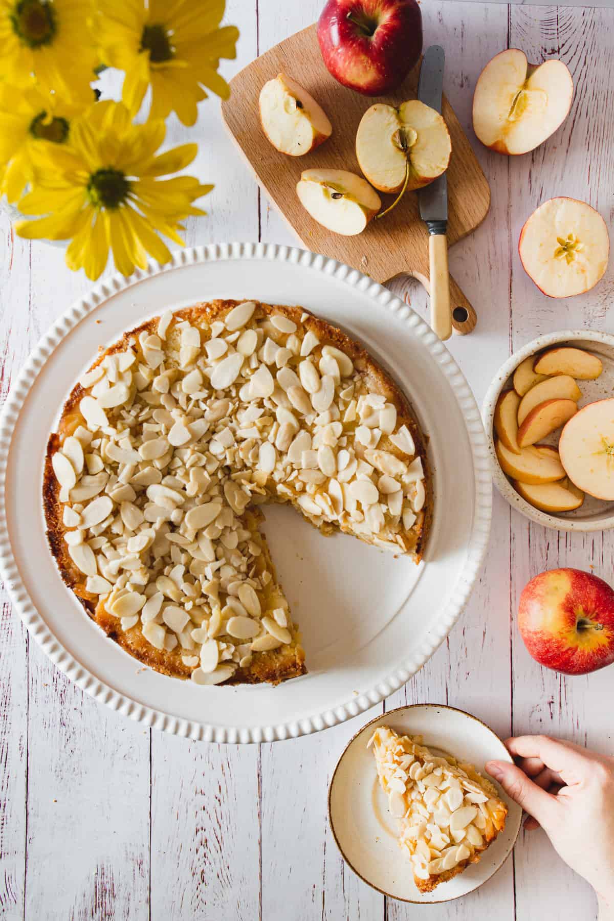 overhead view of gluten free apple cake with hand holding a slice on a plate
