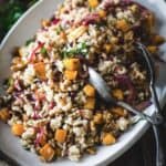 A white plate with a bowl of farro salad topped with butternut squash and wild rice, served with a spoon.