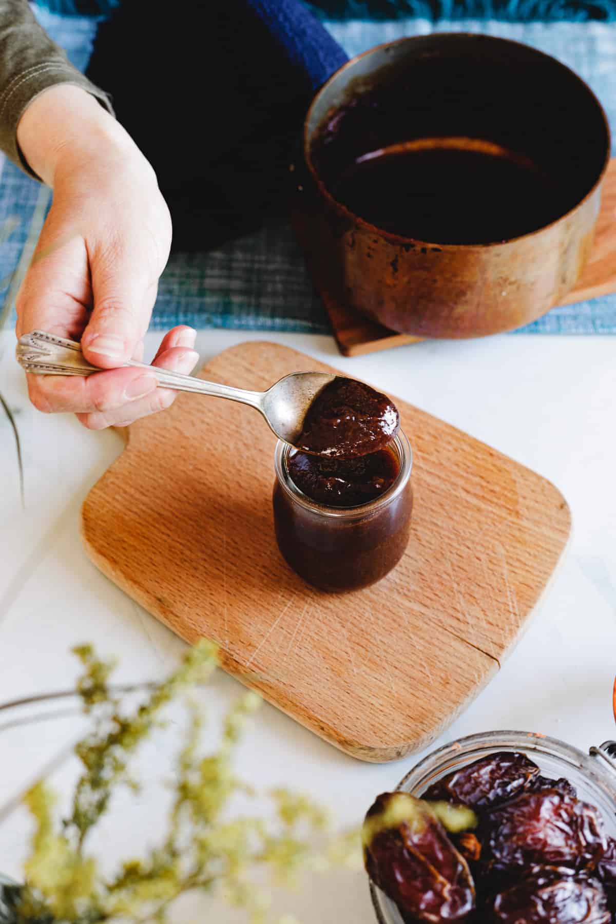 hand lifting a spoon with homemade date syrup over a jar