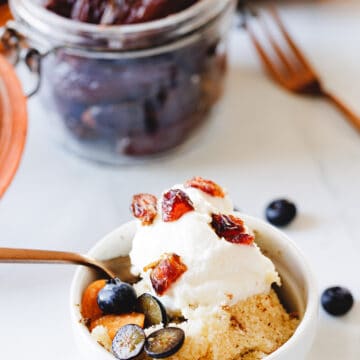 gluten free pouding chomeur in a ramekin with a fork, topped with dates in jar and blueberries and ground cherries
