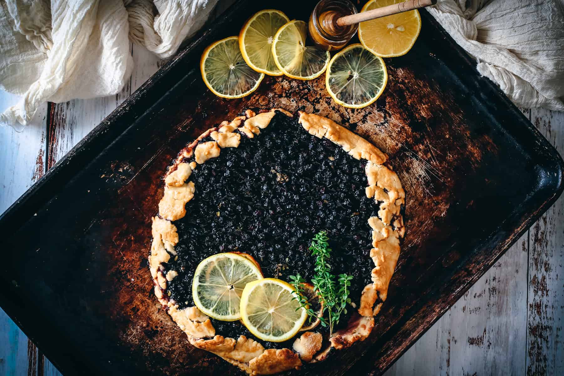 blueberry lemon galette on baking sheet with lemon slices and honey