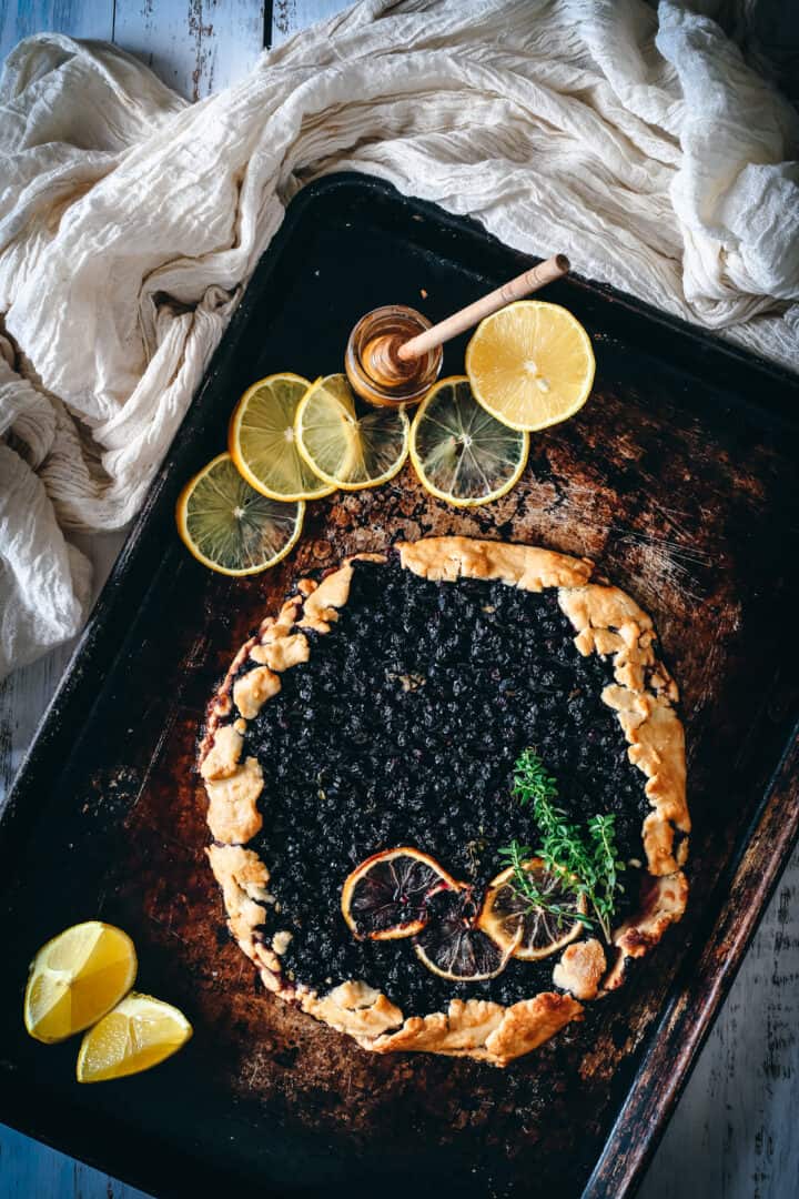 blueberry lemon galette on baking sheet with lemon slices and honey