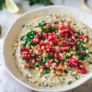 close up on hand lifting piece with Lebanese Baba Ganoush recipe with pomegranate seeds and pine nuts