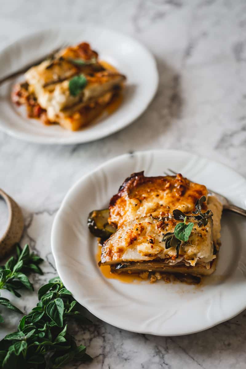 two plates with gluten free vegetarian moussaka with oregano and salt in the front,