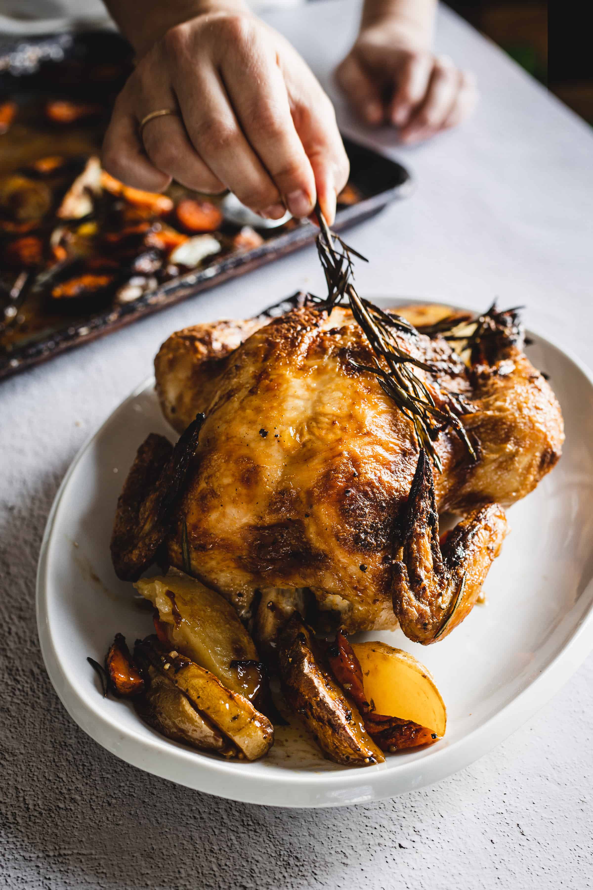 placing a rosemary branch on whole roasted chicken