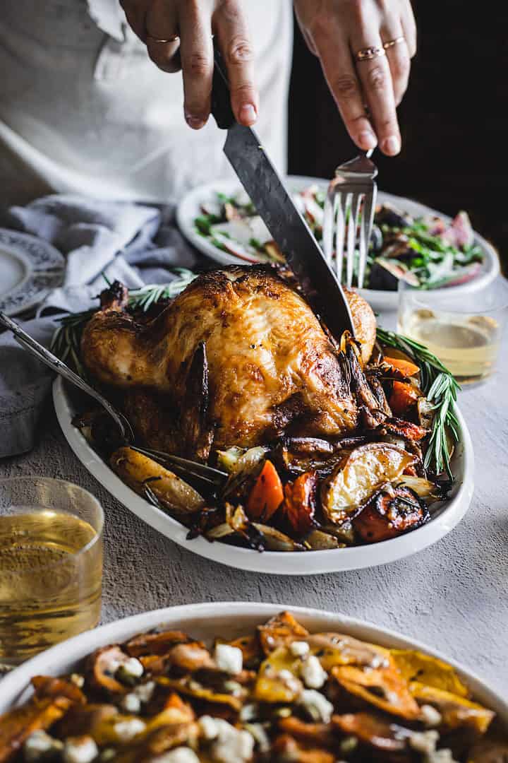 cutting into side view of paprika chicken surrounded by roasted vegetables and side dishes