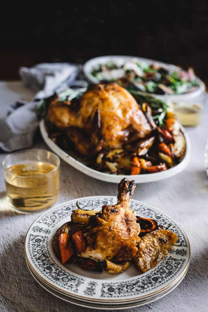 a plate with chicken thigh and veggies with whole table in background